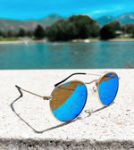 Load image into Gallery viewer, Blue reflective gold rimmed sunglasses for babies and toddlers by a lake
