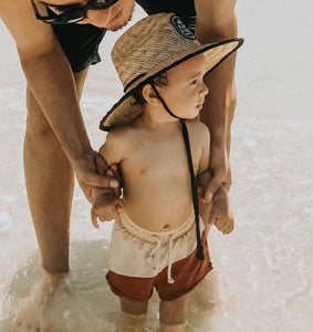 Toddler walking in the water at the beach with a straw beach sun hat