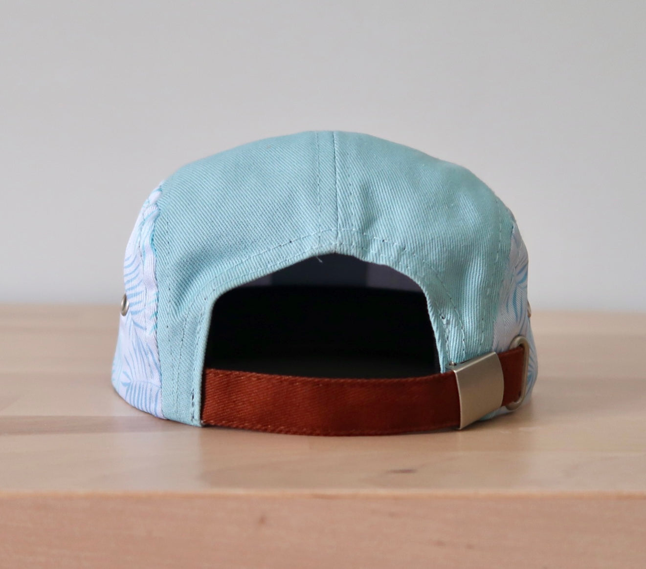 Tropical blue hat featuring aqua beach leaf patterns and a brown adjustable strap