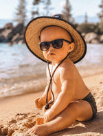 Load image into Gallery viewer, Baby wearing a straw beach sun hat on the beach wearing sunglasses and playing in the sand
