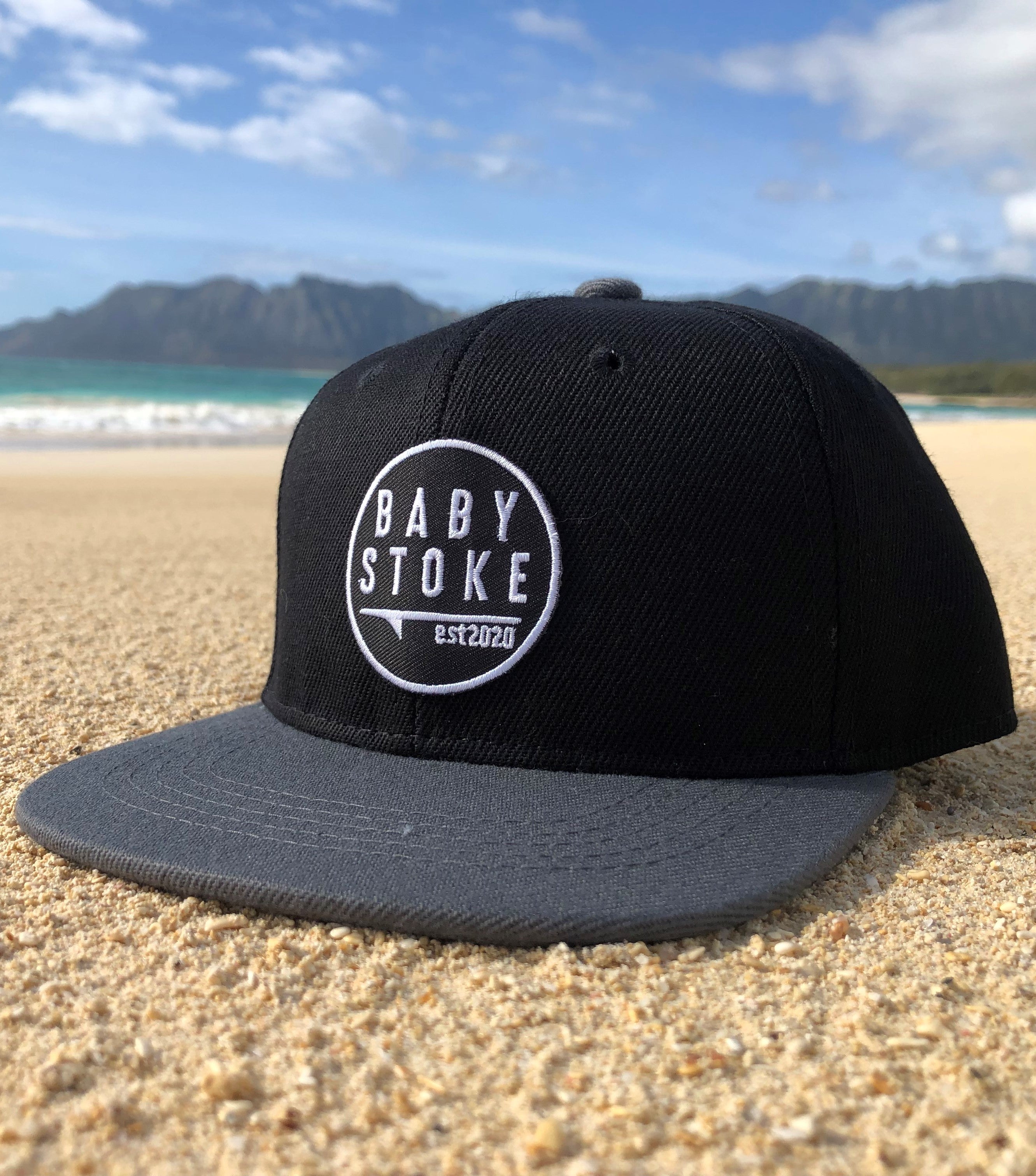 Black snapback with grey bill established 2020 sun hat on the sand at the beach in hawaii for toddlers and babies