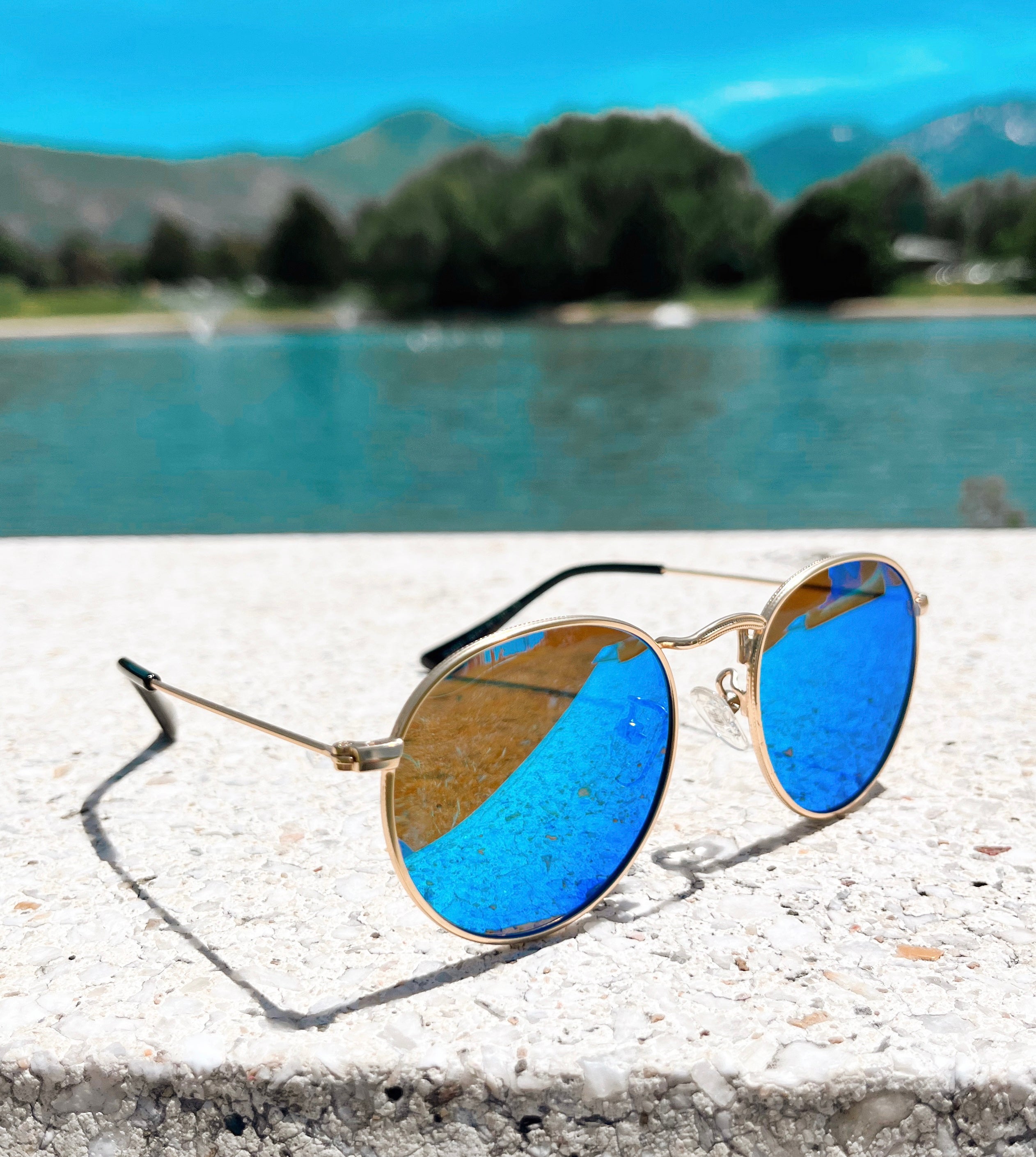 Blue reflective gold rimmed sunglasses for babies and toddlers by a lake
