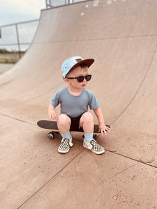 Toddler wearing an ocean blue snap back flat brim hat on an adventure at the skate park with a skateboard