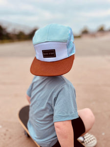 Toddler wearing a sky blue snap back flat brim hat on an adventure at the skate park with a skateboard