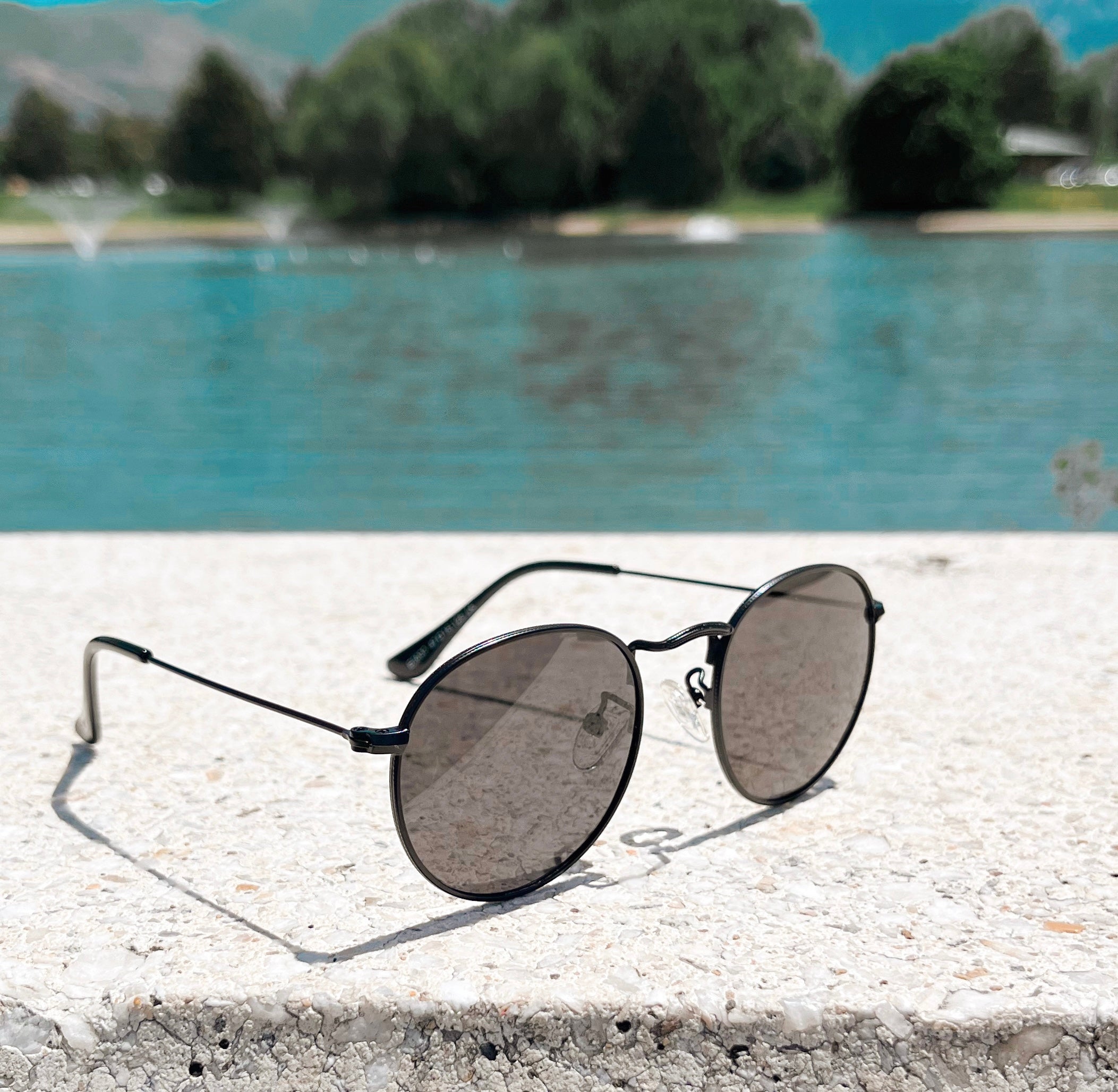 black sunglasses with black rims and lenses to protect babies and toddlers from the sun next to a lake